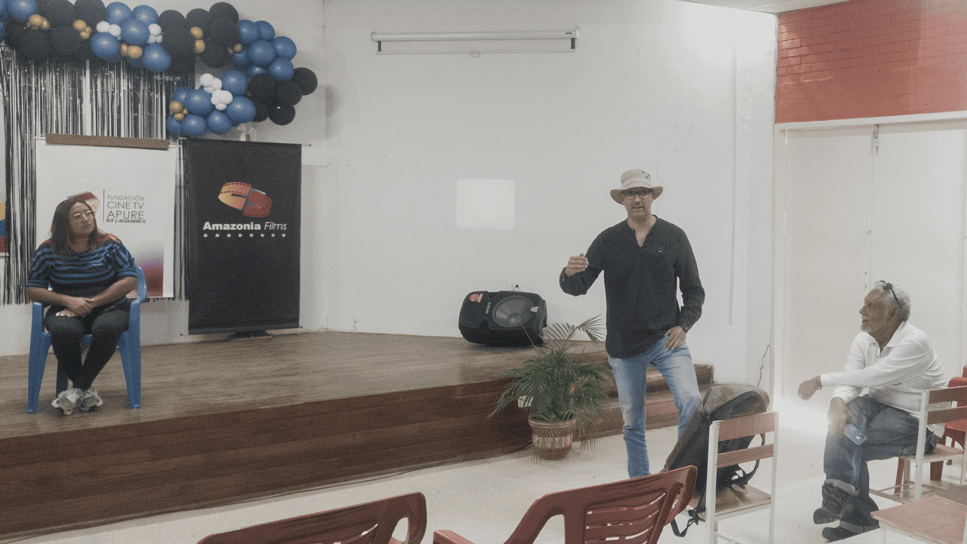 [archivo.jpg], Hombre en una presentación en un espacio cerrado con decoraciones de globos y logotipos de Fundación Cine TV Apure y Amazonia Films, participando en un evento cultural en Apure, Venezuela.